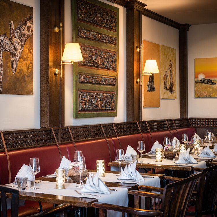 Elegant gedeckte Tische im Restaurantbereich des Park-Hotel Hagenbeck mit afrikanischen Kunstwerken an der Wand