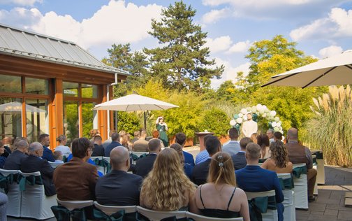 Die Hochzeitsgesellschaft sitzt unter blauem Himmel mit Blick auf den Traualtar und der dahinter liegenden Grünanlage des Park-Hotel Hagenbeck in Hamburg