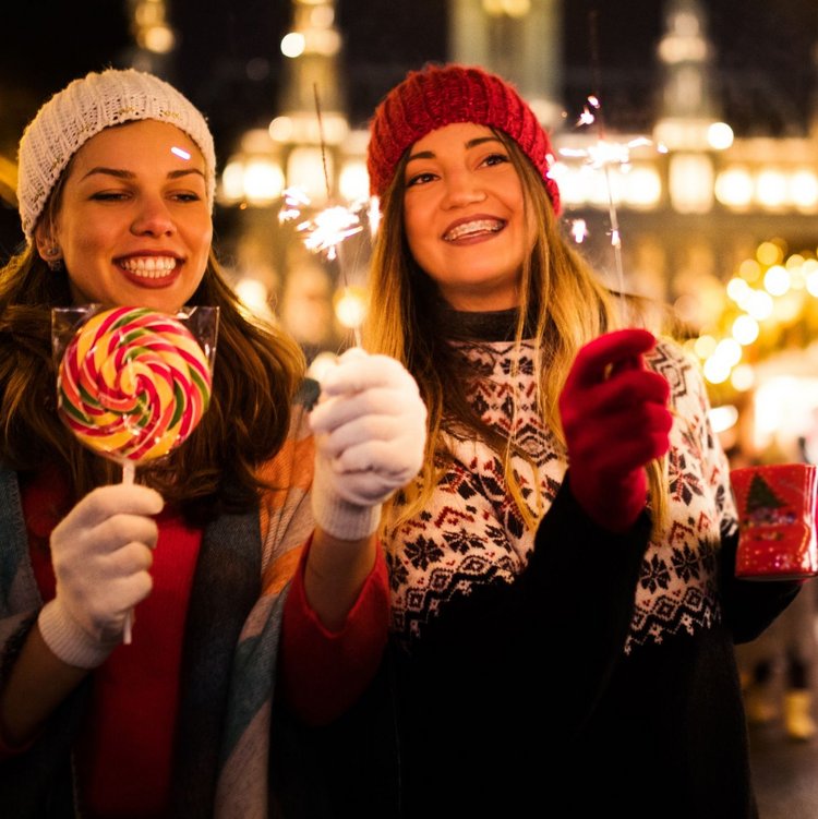 Zwei Frauen mit Süßigkeiten und Heißgetränken auf einem festlich beleuchteten Weihnachtsmarkt