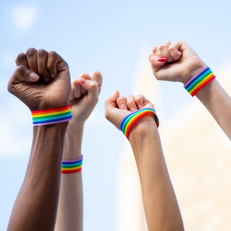 4 Fäuste in den Himmel gestreckt - mit Regenbogen-Armbändern