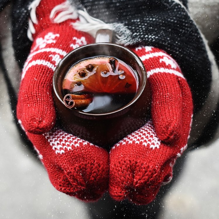 Glühwein auf dem Weihnachtsmarkt – rote Handschuhe halten Tasse mit dampfendem Getränk in winterlicher Stimmung